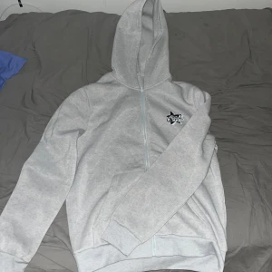 Grå hoodie med dragkedja - Säljer en grå hoodie i mycket bra skick. Den har en dragkedja framtill och en liten logga på bröstet. Med ull inne.
