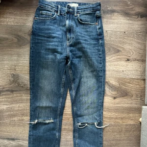 Blå jeans med slitna detaljer - Säljer ett par snygga blå jeans från gina tricot i storlek 34. De är högmidjade och har slitna detaljer vid knäna för en trendig look. 🕺