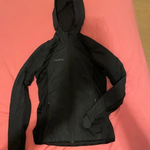 Svart vindjacka från Craft - Säljer en svart vår/höst jacka från Craft i mycket bra skick. Jackan har en dragkedja framtill och en praktisk huva. Perfekt för höst och vår, med långa ärmar och en slim passform. Idealisk för träning eller vardagsbruk. Passar både killar och tjejer, priser går alltid att diskutera🤩Passar även tjejer i storlek S