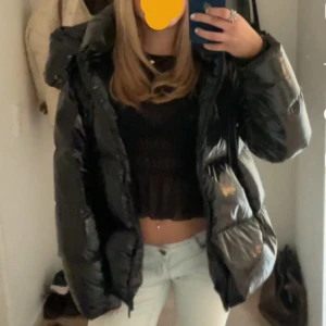 Svart pufferjacka - En jättesnygg svart pufferjacka från Tommy Hilfiger som är perfekt för kalla dagar. Jackan har en glansig yta och är i bra skick med endast en liten defekt som inte syns.  