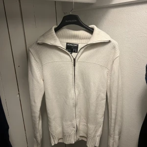 Vit stickad fullzip  - Säljer en snygg vit stickad tröja. Den har en dragkedja framtill och en ribbad krage. Tröjan är i mycket bra skick :)