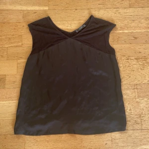 Svart v-ringad T-shirt - Säljer en stilren svart topp med ett satin material på framsidan. Perfekt för både vardag och festliga tillfällen. Toppen har en enkel design med en v-ringad hals och en lös passform. Ett mångsidigt plagg som passar till det mesta i garderoben.