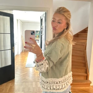 Grön jacka med pom-pom detaljer - Säljer en superfin grön jacka med unika pom-pom detaljer längs ärmar och nederkant. Perfekt för att piffa upp vilken outfit som helst! Jackan har en loose passform och är långärmad. Perfekt för vår och sommar. Säljer för att den är för liten för mig, ganska bra skick då jag köpte den på sellpy för längesen. 