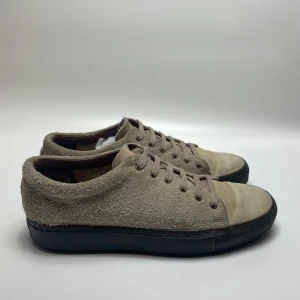 Acne studios skor - Säljer ett par snygga beige sneakers. De har en klassisk design med snörning och en svart sula som ger en cool kontrast. Perfekta för både vardag och fest! Skorna är i bra skick med lite slitage på tån.