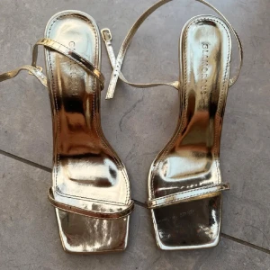 Guldiga klackar 9cm  - Guldiga klackar och smala remmar. Använda en gång, fint skick. Skulle dock inte rekommendera till personer med bred fot därför jag säljer dom tyvärr. Men passformen är fin och bra i storlek