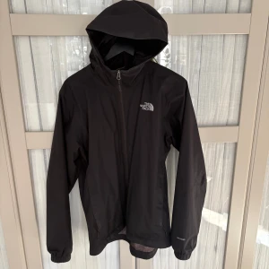 Svart regnjacka från The North Face - Säljer en stilren svart regnjacka från The North Face. Jackan har en praktisk huva och dragkedja framtill. Perfekt för regniga dagar och håller dig torr och bekväm. Passar bra till både vardag och utomhusaktiviteter.