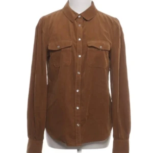 Brun manchester skjorta - Snygg brun manchester skjorta med långa ärmar och klassisk krage. Skjortan har knappar framtill och två bröstfickor med lock. Perfekt för en stilren look.