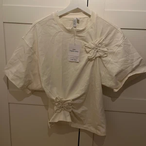 Vit t-shirt med rosetter - Säljer en stilren vit t-shirt från Zara med unika rosettdetaljer på bröstet och nedtill. Säljs inte länge. Med prislappen kvar