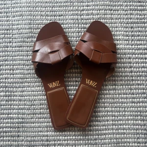 Bruna sandaler från Zara - Snygga bruna sandaler från Zara med flätad design. Perfekta för sommardagar med en stilren look. Sandalerna har en öppen tå och är tillverkade i ett skinnliknande material.