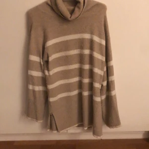 Beige och vit randig polotröja från Lindex - Mysig beige polotröja från Lindex med vita ränder. Tröjan har långa ärmar och en bekväm passform, perfekt för kyligare dagar. Den är tillverkad i ett mjukt material som känns skönt mot huden. Denna tröja är inte så flitigt använt men det är den absolut skönaste och gosigaste tröjan jag haft på mig!!❤️ passar en xs-M