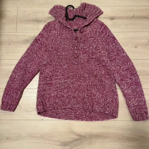 Lila stickad tröja med knappar - Mysig lila stickad tröja med knappar framtill och en hög krage. Perfekt för kyliga dagar. Tröjan har långa ärmar och en avslappnad passform.