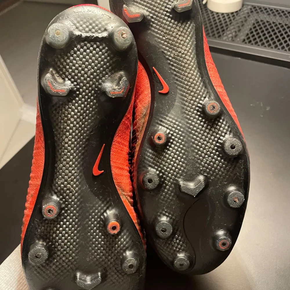 Säljer ett par röda Nike Mercurial fotbollsskor med hög ankelkrage och svart swoosh-logga. Skorna har en strömlinjeformad design och är perfekta för snabba rörelser på planen. De är designade för att ge bra grepp och kontroll.. Kengät.