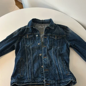 Jeansjacka från Only - Snygg jeansjacka från Only i klassisk blå denim. Jackan har knappar framtill och två bröstfickor med lock. Perfekt för en avslappnad stil och passar bra till både jeans och kjol.