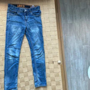 Blå jeans från Levi's - Snygga blå jeans från Levi's med klassisk femficksdesign och knappgylf. Perfekta för en avslappnad stil. De har en smal passform och är tillverkade i slitstarkt denim.
