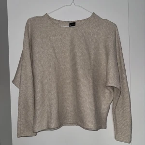 Beige stickad tröja från Vero Moda - Säljer en stilren beige stickad tröja från Gina Tricot. Tröjan har en avslappnad passform med långa pingvinärmar och en rund halsringning. Perfekt för kyligare dagar och enkel att matcha med olika outfits.