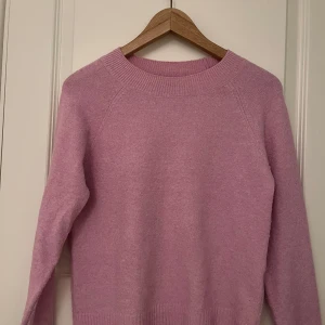 Ljusrosa stickad tröja - Mysig ljusrosa stickad tröja med rund halsringning och långa ärmar. Perfekt för kyligare dagar och ger en mjuk och bekväm känsla. Passar bra till både jeans och kjol för en avslappnad look.