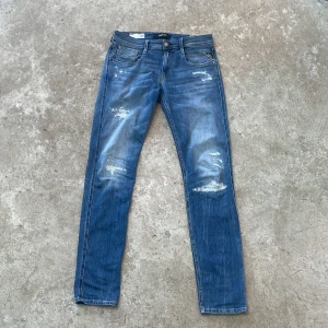 Blå jeansbyxor från Replay - Snygga blå jeansbyxor från Replay, modell Anbass. De har en slim fit passform och är dekorerade med slitningar för en trendig look. Perfekta för en avslappnad stil. Väldigt bra skick och knappast använda, var inte rädda för att ställa frågor 👍