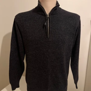 Mörkgrå stickad tröja från Cricket - Säljer en stilren mörkgrå stickad tröja från Cricket med dragkedja vid halsen. Tröjan har långa ärmar och en ribbad krage samt muddar vid ärmslut och nederkant. Perfekt för kyligare dagar.
