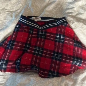 Rutig kjol från Hampton Republic - Snygg rutig kjol i rött och svart från Hampton Republic. Kjolen har en dragkedja i sidan och ett elastiskt midjeband med ränder. Perfekt för en stilren look! Lite nopprig men annars i fint skick 