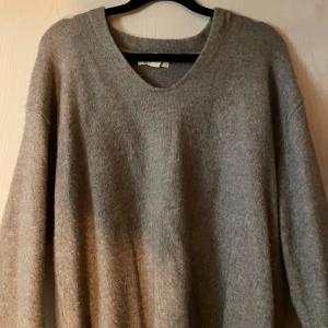 Grå stickad tröja - Mysig grå stickad tröja med v-ringning och långa ärmar. Perfekt för kyliga dagar och enkel att matcha med olika outfits.