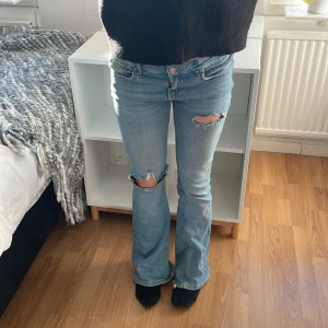 Blå bootcut jeans med slitningar - Säljer ett par lågmidjade blå bootcut jeans med slitningar på knäna. 