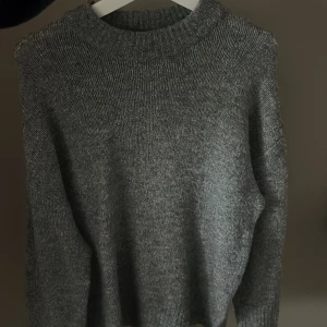 Grå stickad tröja - Säljer en mysig grå stickad tröja med ribbad hals och långa ärmar. Perfekt för kyliga dagar och enkel att matcha med olika outfits. Passar både till vardags och mer avslappnade tillfällen.