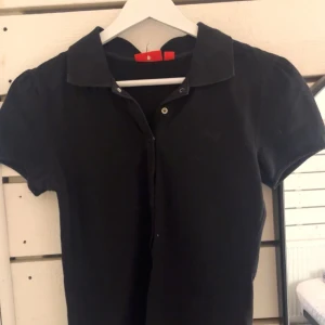 Svart polotopp från Puma - Säljer en stilren svart polotopp från Puma. Toppen har korta ärmar och en klassisk krage med knappar på. Mycket bekväm tröja.