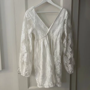 Vit blommig klänning med spetsdetaljer - Säljer en vacker vit klänning med blommigt spetsmönster och v-ringning. Klänningen har långa ärmar och en luftig passform, perfekt för sommarens festligheter. Den är tillverkad i ett lätt och bekvämt material som ger en romantisk känsla. Perfekt för att känna sig extra fin! 🌸