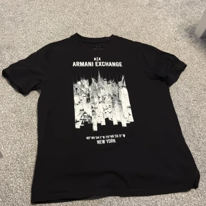 Svart t-shirt från Armani Exchange - Snygg svart t-shirt från Armani Exchange med ett coolt New York-tryck i vitt på framsidan. Perfekt för en stilren och modern look.