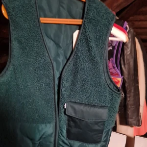 Grön fleeceväst med dragkedja - Säljer en grön fleeceväst med dragkedja och praktiska fickor. Perfekt för kyligare dagar och ger en skön och avslappnad stil. Västen har en normal passform och är idealisk för lager-på-lager.