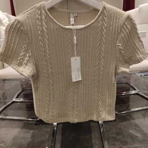Beige stickad topp från NLY Trend - Säljer en beige stickad topp från NLY Trend med kabelstickat mönster. Toppen är croppad och har korta ärmar, perfekt för en stilren look. Passar bra till både jeans och kjol. 🌟