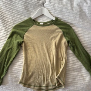 Beige och grön långärmad tröja - Säljer en beige och grön långärmad tröja med kontrasterande ärmar. Tröjan har en rund halsringning och är perfekt för en avslappnad stil. Tillverkad i ett mjukt material som känns skönt mot huden.