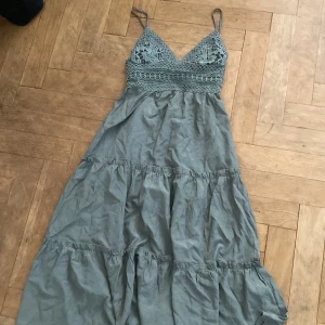 Grön klänning med spetsdetaljer - Charmig grön klänning med spetsdetaljer på överdelen och smala axelband. Klänningen har en v-ringad design och volanger som ger en romantisk känsla. Perfekt för sommarens varma dagar.