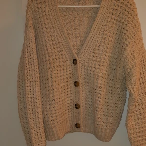 Beige stickad kofta från Esmara - Mysig beige stickad kofta från Esmara med stora knappar framtill. Koftan har en luftig stickning och långa ärmar, perfekt för kyliga dagar. Den har en avslappnad passform och ribbade muddar vid ärmslut och nederkant.