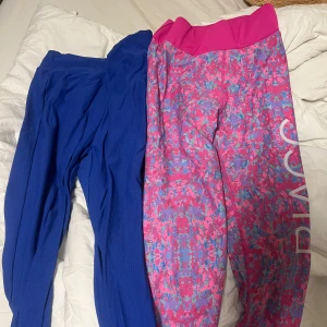 Två par färgglada leggings - Säljer två par leggings. Ett par är blåa med ribbad textur och det andra paret är rosa med blått och rosa mönster samt texten 'DIACC' längs benet. Perfekta för träning eller en färgglad vardag.