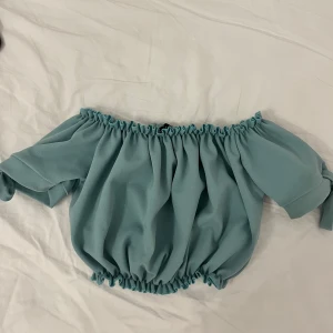 Turkos offshoulder topp - Säljer en söt turkos offshoulder topp med elastiska kanter och knytband på ärmarna. Perfekt för en somrig look!
