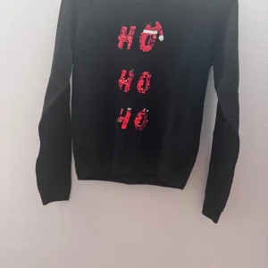 Svart jultröja med paljetter - Säljer en svart jultröja med paljetter som bildar texten 'HO HO HO' i rött, grönt och vitt. Tröjan har långa ärmar och är perfekt för julfirandet. Paljetterna kan vändas för att ändra färg på texten.är i storlek 158/164