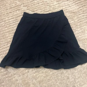 Marinblå volangkjol från ONLY - Snygg svart omlottkjol från ONLY med volangdetaljer. Jätte fin och bekväm, den är perfekt till i sommar. Färgen är typ en blandning av marinblå och svart❤️