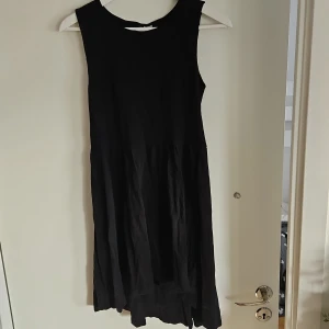 Svart ärmlös klänning - Snygg svart ärmlös klänning med en luftig passform. Längre baktill. Perfekt för en stilren look. Klänningen har en enkel design som gör den lätt att matcha med olika accessoarer.