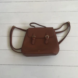 Brun axelväska från Anna Field - Snygg brun axelväska från Anna Field med justerbara remmar och stilrena spännen. Väskan har en praktisk dragkedja inuti och en elegant design som passar perfekt för alla tillfällen. Perfekt för dig som vill ha både stil och funktionalitet i en väska.