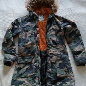 Camouflage parkajacka med fluffigt foder - Använd men i väldigt bra skick,liite sliten precis vid kanten på ärmarna på några ställen men inget som syns om man inte tittar precis där.  Håller värmen förvånansvärt bra utan att kännas klumpig eller tjock, och är slit-tålig.( Jag har överlevt dunder-vintrar i mellersta Norrland med denna,och jag har extremt svårt att hålla värmen annars..) Dubbel dragkedja som kan öppnas uppe och nere. Säljer pga det är dags för lite variation och har ej plats att spara allt😝