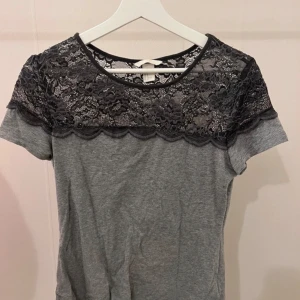 T-shirt med spets  - Trendig grå  t-shirt med spets uppe. Normal i storlek, passar S-M. Nyskick, knappt använd!💕 fritt fram att trycka köp nu så hör jag av mig!💕