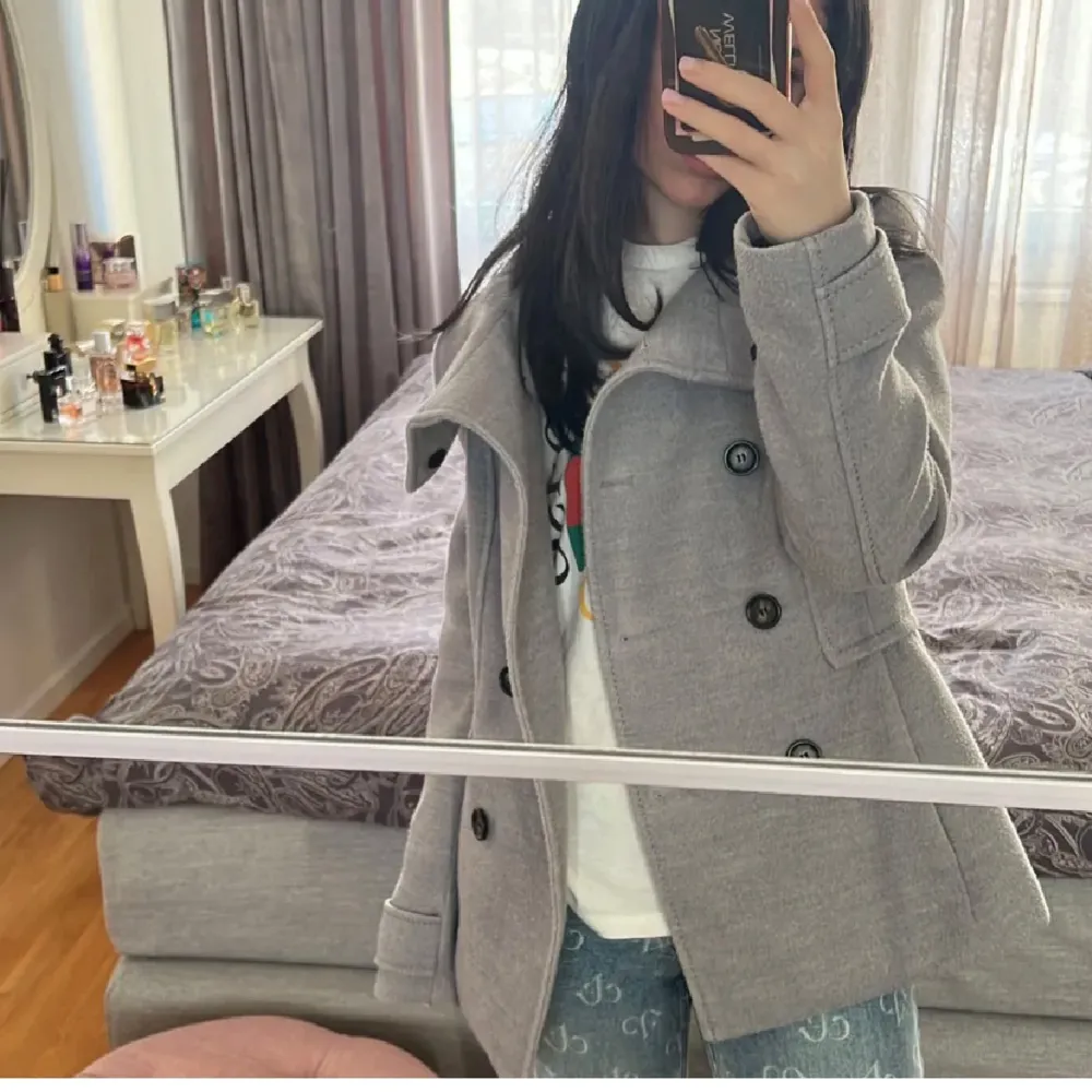 SĂ€ljer en snygg grĂ„ kappa med stora knappar framtill. Den har en stilren design med en bred krage och Ă€r perfekt för höst och vĂ„r. Jackan Ă€r lĂ„ngĂ€rmad och ser ut att vara i bra skick. Perfekt för att hĂ„lla sig varm och stilren under kyligare dagar.đ. Takit.
