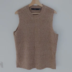Beige stickad väst från Vero Moda - Säljer en snygg beige stickad väst från Vero Moda. Perfekt för lager-på-lager under höst och vinter. Västen har en normal passform och är supermjuk och bekväm. Den har en ribbad kant vid halsen och små slitsar på sidorna för extra stil. Passar perfekt till både vardag och fest!