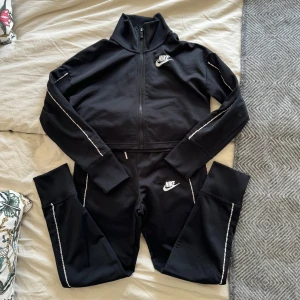Svart träningsset från Nike - Snyggt svart träningsset från Nike till tjej Stl 137-146. Croppad top m. dragkedja och matchande byxor m. fickor.  Perfekt för träning eller en avslappnad dag. Setet är lite nopprigt på några ställen därav pris. Hämtas på Hägerstensåsen eller ök 🖤