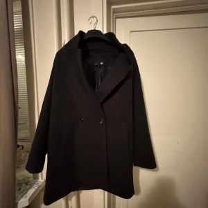 Svart rock från 157 - Säljer en stilren svart rock från 157 i storlek M. Rocken har en klassisk design med knappar framtill och långa ärmar. Perfekt för höst och vinter för en elegant look.