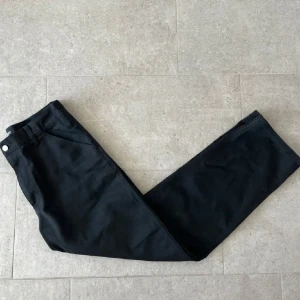 Svarta byxor från Carhartt - Säljer ett par svarta byxor från Carhartt. De har en klassisk design med raka ben och praktiska bakfickor. Perfekta för en stilren och avslappnad look. Har även lagt upp dem för dem var väldigt långa. Så nu är dem i storlek 30/30. Nypris ligger på ungefär 1200kr