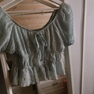 Ljusgrön blus med knytning - Charmig ljusgrön blus med korta ärmar och knytning framtill. Blusen har en luftig passform med volangdetaljer och ett lätt rynkat mönster som ger en romantisk känsla.
