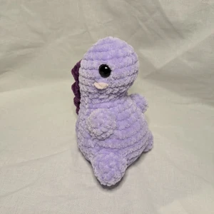 Lila dino🦖 - En lila gullig dino. Den är egenvirkad i ett fluffigt garn. Längd: 14 cm