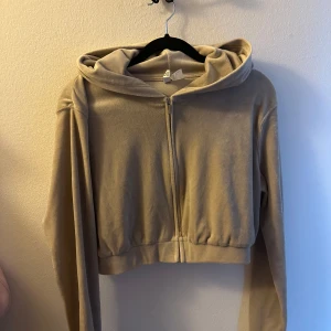Beige croppad hoodie - Säljer en beige croppad hoodie med dragkedja och huva. Den har långa ärmar och är tillverkad i ett mjukt material som ger en skön känsla. Perfekt för en avslappnad stil.
